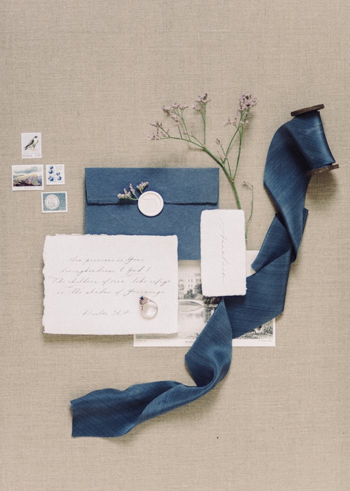 Artistic flat lay of vintage stationery, blue ribbon, and stamps on beige fabric.